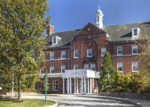 Ornate brick hospital building with a white cupola, surrounded by trees on a sunny day.