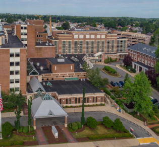 Aerial view of a large, multi-story brick building with a central dome surrounded by additional structures and landscaping.