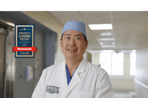 Smiling doctor in white coat and surgical cap wearing "America's Leading Doctors" Newsweek award.